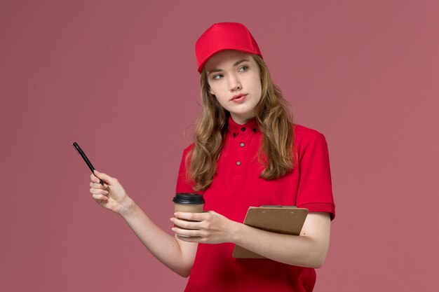 vrouwelijke koerier in rood uniform met koffiepen en blocnote op roze, uniforme baan van de dienstverlener