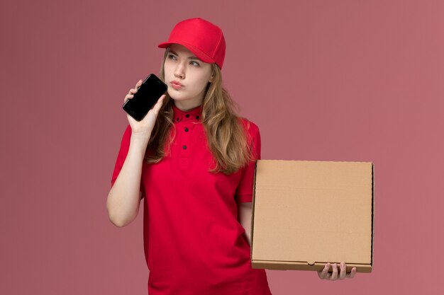vrouwelijke koerier in rood uniform met telefoonvoedselbox op lichtroze, baan uniforme dienstverlener levering