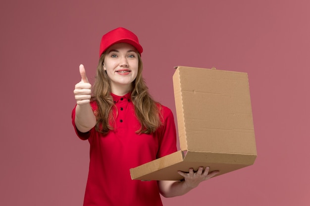 vrouwelijke koerier in rood uniform met voedseldoos en lachend op roze, uniforme dienstverlener