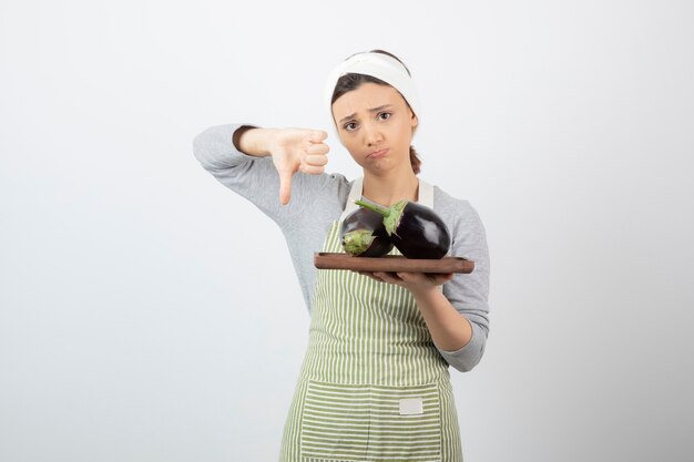 vrouwelijke kok die een bord met grote aubergines vasthoudt en duimen naar beneden geeft.