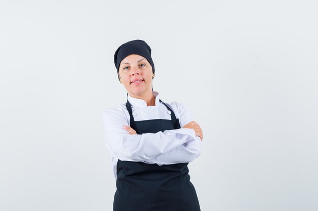 Vrouwelijke kok in uniform, schort die zich met gekruiste armen bevindt en er zelfverzekerd uitziet, vooraanzicht.