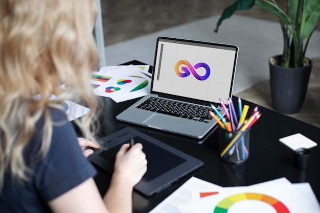 Vrouwelijke logo-ontwerper werkt aan haar tablet die is aangesloten op een laptop