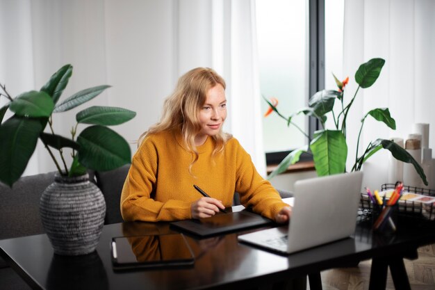Vrouwelijke logo-ontwerper werkt aan haar tablet die is aangesloten op een laptop
