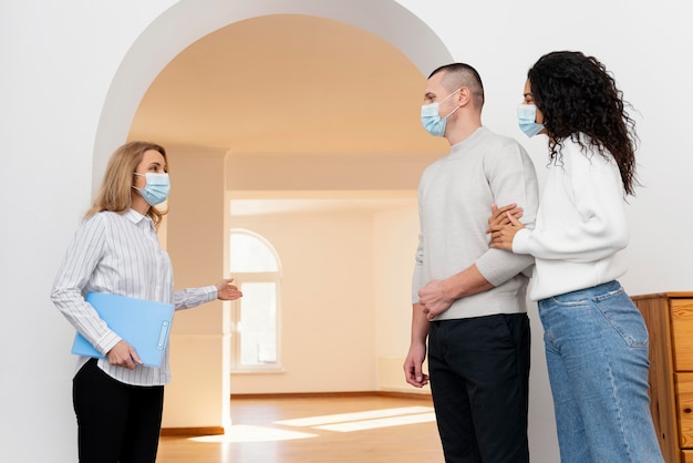 Vrouwelijke makelaar met medisch masker dat paar nieuw huis toont