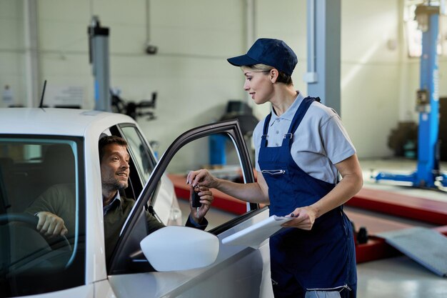 Vrouwelijke monteur die autosleutel geeft aan haar klant in autoreparatiewerkplaats