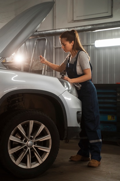 Vrouwelijke monteur die in de winkel aan een auto werkt