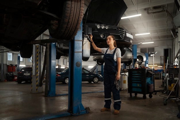 Vrouwelijke monteur die in de winkel aan een auto werkt