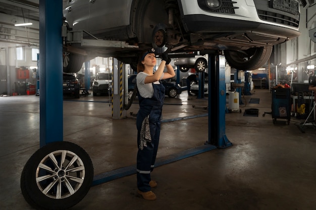 Vrouwelijke monteur die in de winkel aan een auto werkt