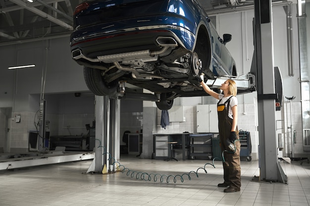 Vrouwelijke monteur observeren onderstel van opgeheven auto.