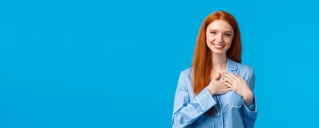 Vrouwelijke mooie roodharige vrouw met lang rood haar in pyjama's houdt handen op het hart en glimlacht