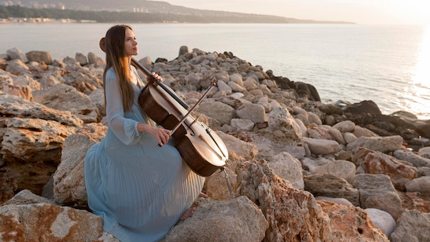 Gratis foto vrouwelijke musicus die cello speelt bij zonsondergang