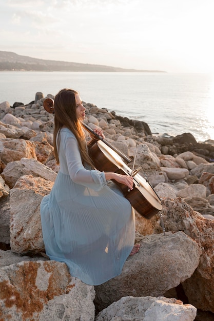 Vrouwelijke muzikant cello buiten spelen bij zonsondergang