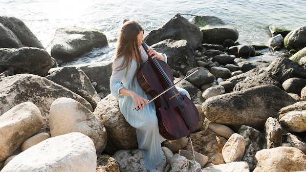 Vrouwelijke muzikant die op rotsen cello speelt door de oceaan