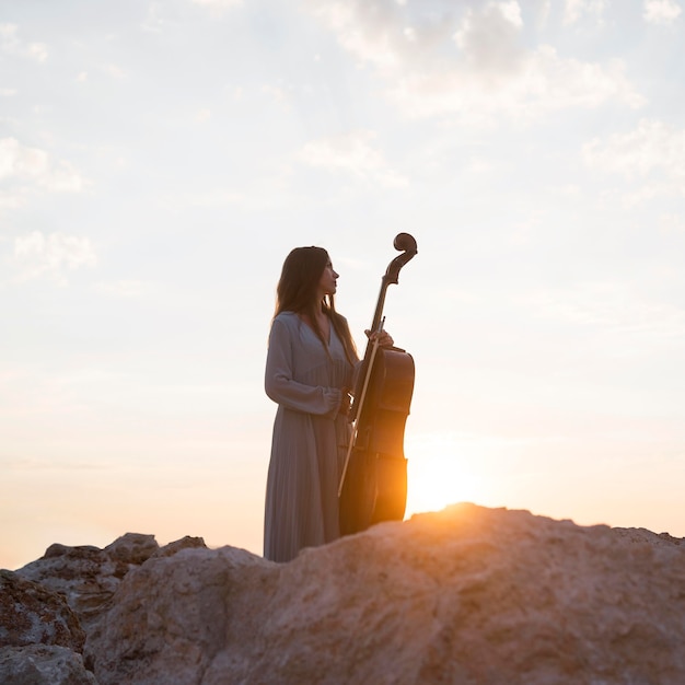 Vrouwelijke muzikant met cello buiten bij zonsondergang