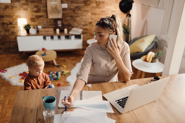 Vrouwelijke ondernemer aan de telefoon terwijl ze thuis met haar zoon is