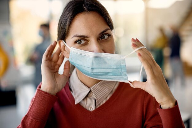 Vrouwelijke ondernemer die een gezichtsmasker opdoet terwijl hij op kantoor werkt