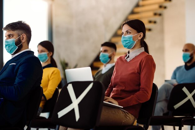 Vrouwelijke ondernemer die laptop gebruikt en een gezichtsmasker draagt tijdens een zakelijk seminar