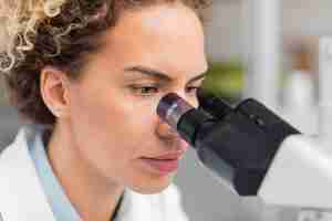 Gratis foto vrouwelijke onderzoeker die in het laboratorium door microscoop kijkt