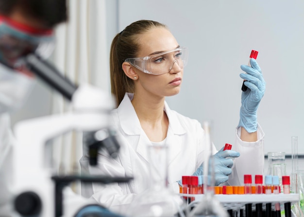 Vrouwelijke onderzoeker in het laboratorium met reageerbuizen en veiligheidsbril naast mannelijke collega