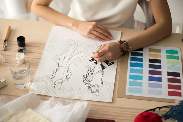 Vrouwelijke ontwerperhanden die het schema van het borduurwerkpatroon op manierschets schilderen