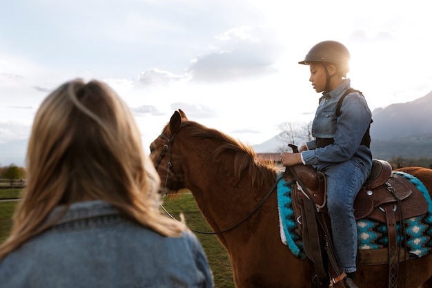 Gratis foto vrouwelijke paardensportinstructeur die kind leert paardrijden