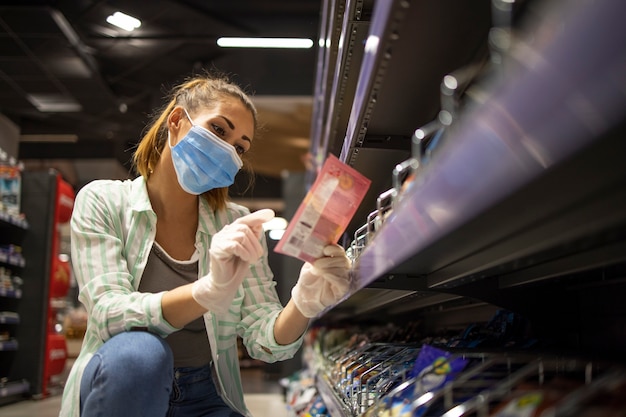 Vrouwelijke persoon met masker en handschoenen die voedsel in supermarkt kopen