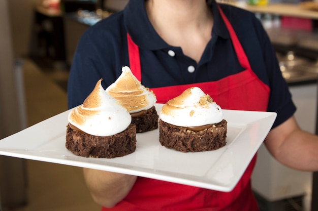 Gratis foto vrouwelijke serveerster die chocoladetaart met slagroom in dienblad houdt