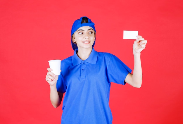 Vrouwelijke serviceagent in blauw uniform die een kopje drank houdt en haar visitekaartje presenteert.