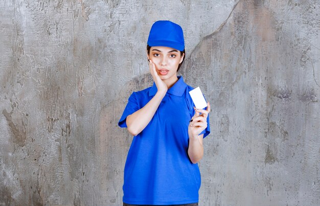 Vrouwelijke serviceagent in blauw uniform presenteert haar visitekaartje en ziet er verward of attent uit.