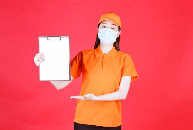 Vrouwelijke serviceagent in oranje kleuruniform en masker die het projectblad demonstreert en ernaar wijst.