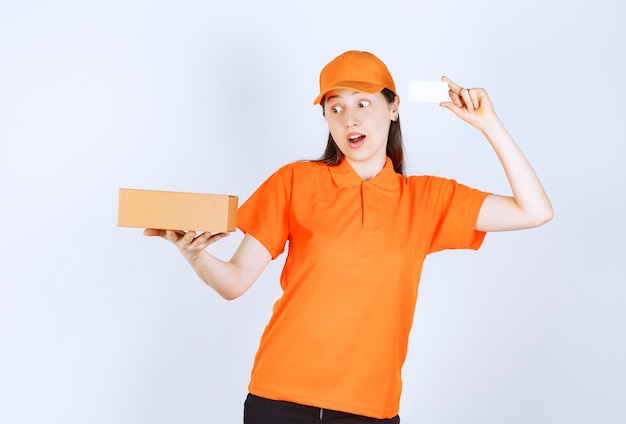 Vrouwelijke servicemedewerker in oranje kleur dresscode die een kartonnen doos vasthoudt en haar visitekaartje presenteert.