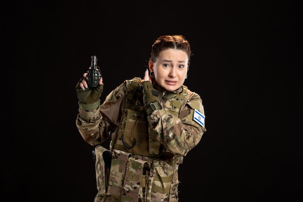 Vrouwelijke soldaat in camouflage met granaat in haar handen op zwarte muur