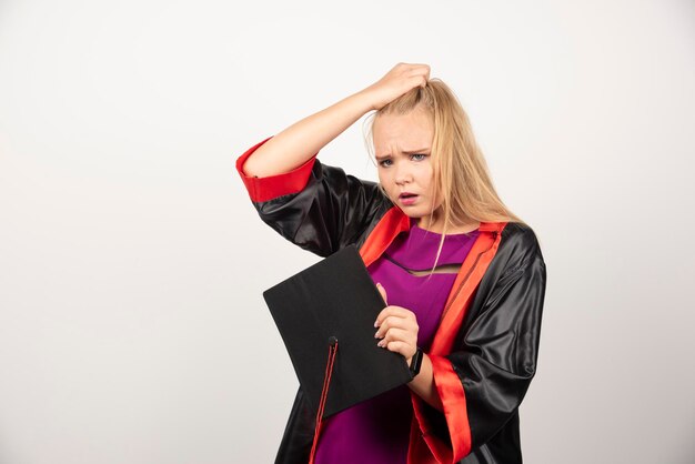 Vrouwelijke student die in toga haar GLB op witte achtergrond houdt. Hoge kwaliteit foto