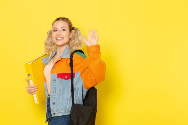 vrouwelijke student jong in moderne kleding gewoon poseren met glimlach bedrijf bestand zwaaien op geel