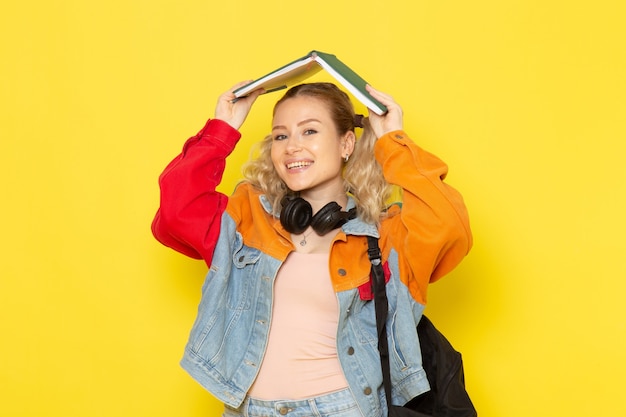 Gratis foto vrouwelijke student jong in moderne kleding met copybooks lachend op geel