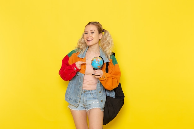 Vrouwelijke student jong in moderne kleding met een wereldbol met een glimlach op geel