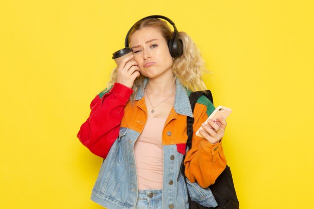 vrouwelijke student jongelui in moderne kleding koffie en telefoon op geel te houden