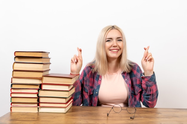 Vrouwelijke student zit gewoon met boeken die haar vingers op wit kruisen