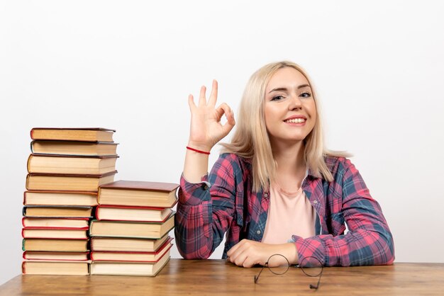 Gratis foto vrouwelijke student zit gewoon met verschillende boeken lachend op wit