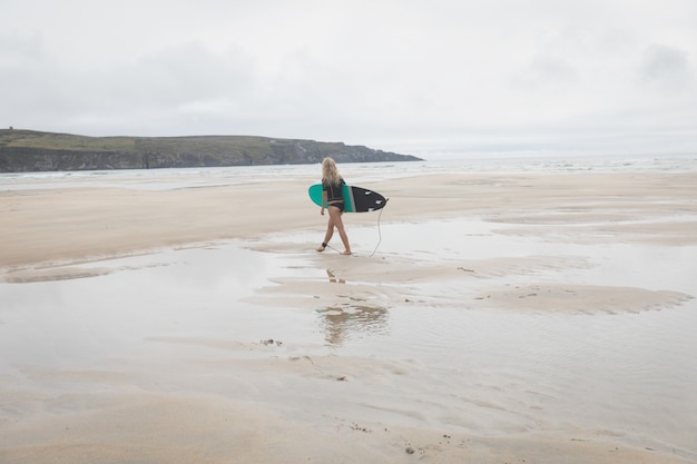 Vrouwelijke surfer die op een strand met surfplank loopt