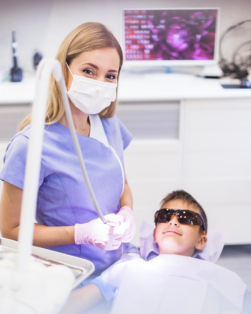 Vrouwelijke tandarts die zich dichtbij jongen bevindt die veiligheids beschermende glazen draagt