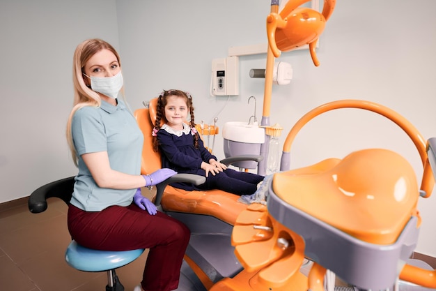 Vrouwelijke tandarts zit naast schattig klein meisje