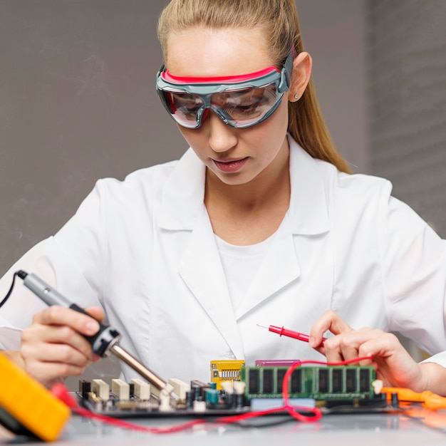 Vrouwelijke technicus met soldeerbout en elektronikamoederbord