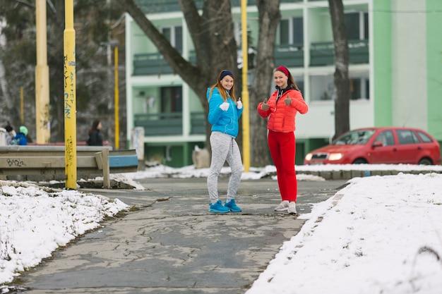 Vrouwelijke trainer twee die zich op straat in wintertijd bevinden die duim op teken omhoog geven