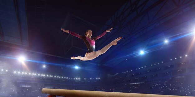Vrouwelijke turnster doet een ingewikkelde truc op gymnastiek-evenwichtsbalk in een professionele arena