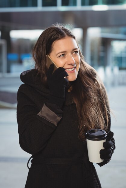 Vrouwelijke uitvoerende praten op mobiele telefoon terwijl het hebben van koffie