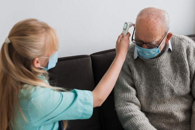 Vrouwelijke verpleegster die de temperatuur van de oude man controleert