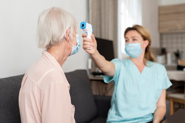 Vrouwelijke verpleegster die de temperatuur van de oudere vrouw controleert