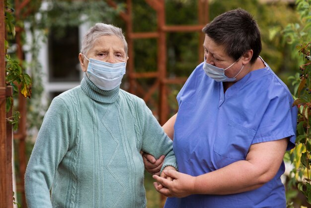 Vrouwelijke verpleegster die oudere vrouw met medisch masker behandelt