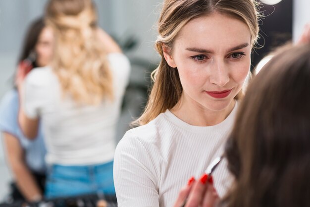 Vrouwelijke visagiste die make-up op cliënt zet